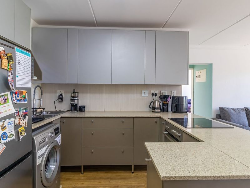 Modern open-plan kitchen featuring sleek grey cabinetry, stone countertops, integrated hob, and built-in oven, seamlessly flowing into the adjacent living area.