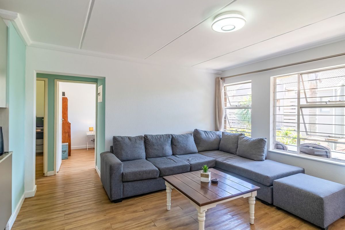 A bright living room featuring laminate flooring, large windows with aluminium frames, and a neutral color palette, providing a comfortable and functional living space.