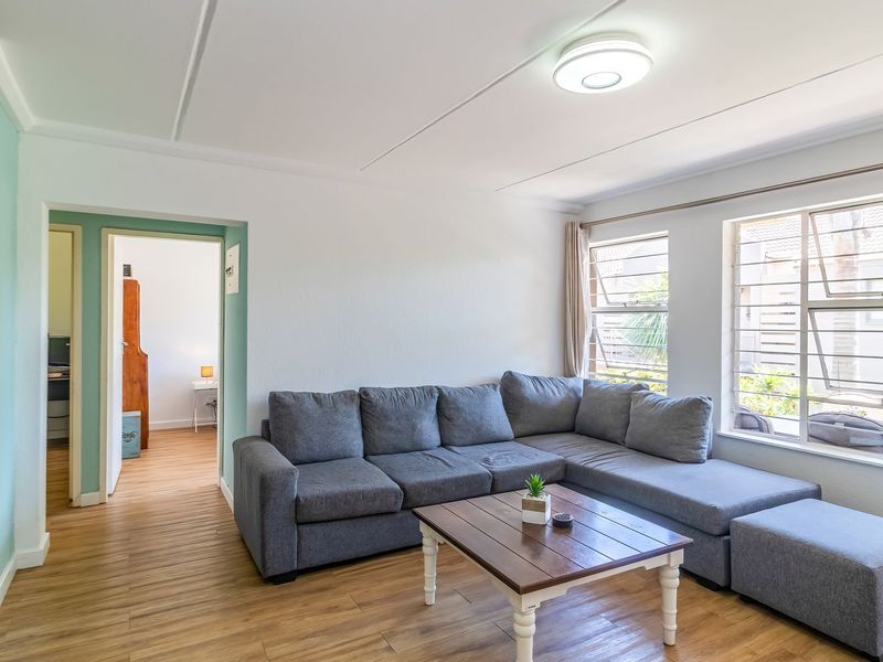 A bright living room featuring laminate flooring, large windows with aluminium frames, and a neutral color palette, providing a comfortable and functional living space.