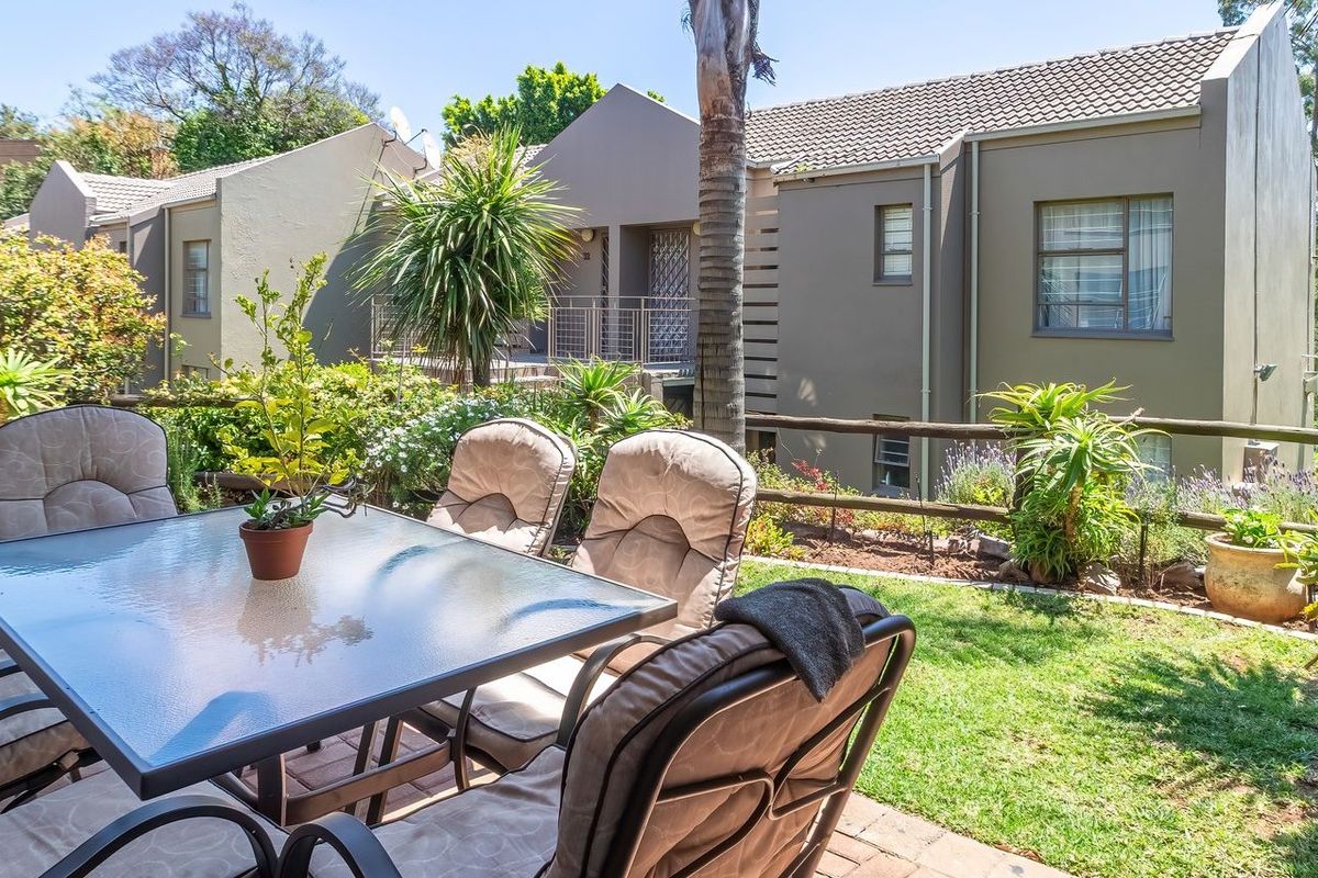 A well-maintained rear garden featuring a paved patio area, established landscaping, and a timber rail fence, set against the backdrop of the residential building.