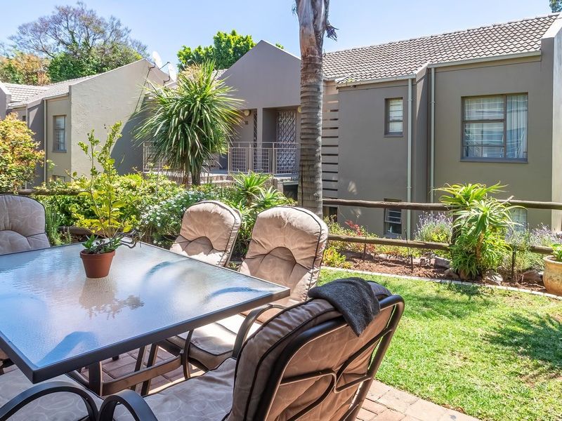 A well-maintained rear garden featuring a paved patio area, established landscaping, and a timber rail fence, set against the backdrop of the residential building.