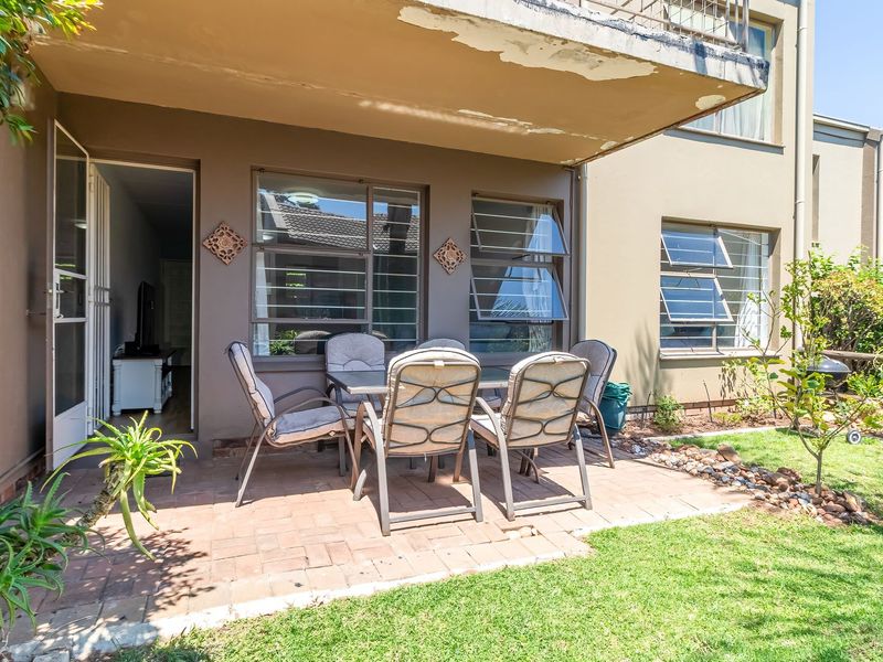 A covered paved patio area with access to the interior, featuring a concrete overhang and adjacent garden space.