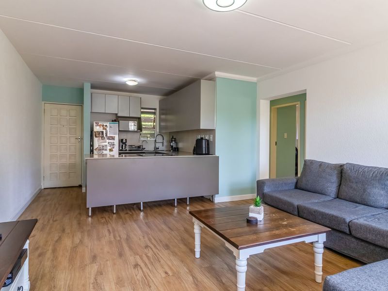 Open-plan living area featuring a functional kitchen with built-in cabinetry and a central island, seamlessly connected to the lounge space with laminate flooring.