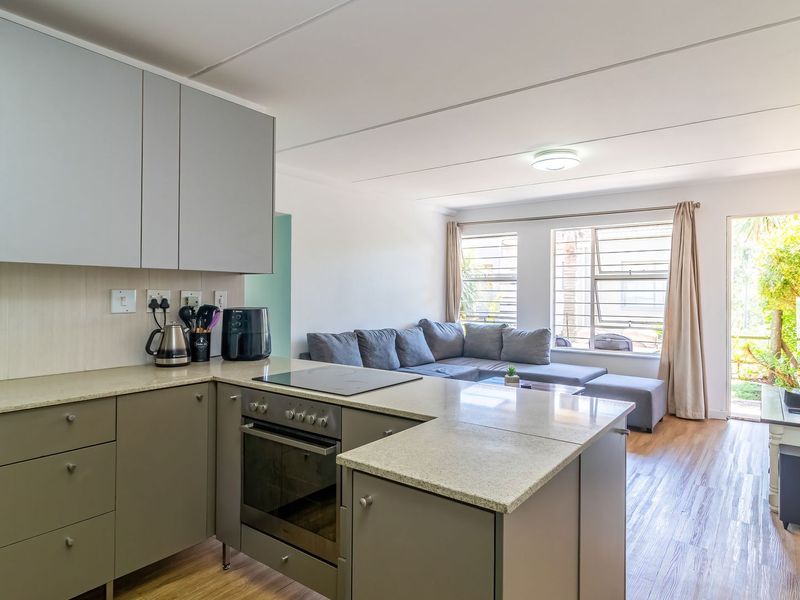 Open-plan living area featuring a modern kitchen with built-in cabinetry, stone countertops, and integrated oven, flowing into a bright lounge with garden access.