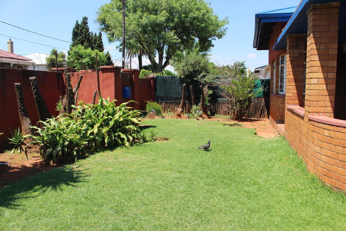 A private rear garden featuring a lawn area, brick boundary walls, and established perimeter landscaping adjacent to the main house structure.