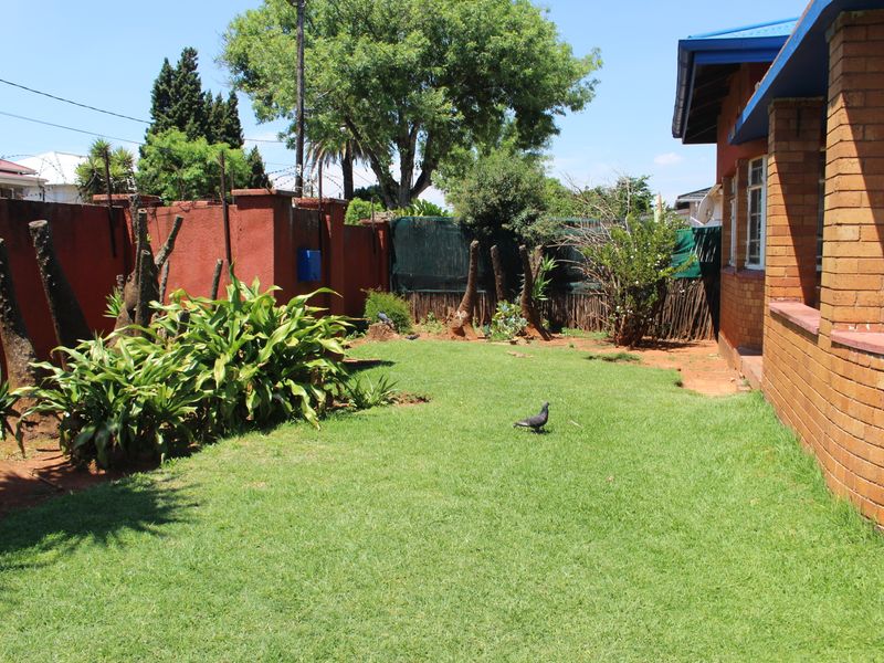 A private rear garden featuring a lawn area, brick boundary walls, and established perimeter landscaping adjacent to the main house structure.