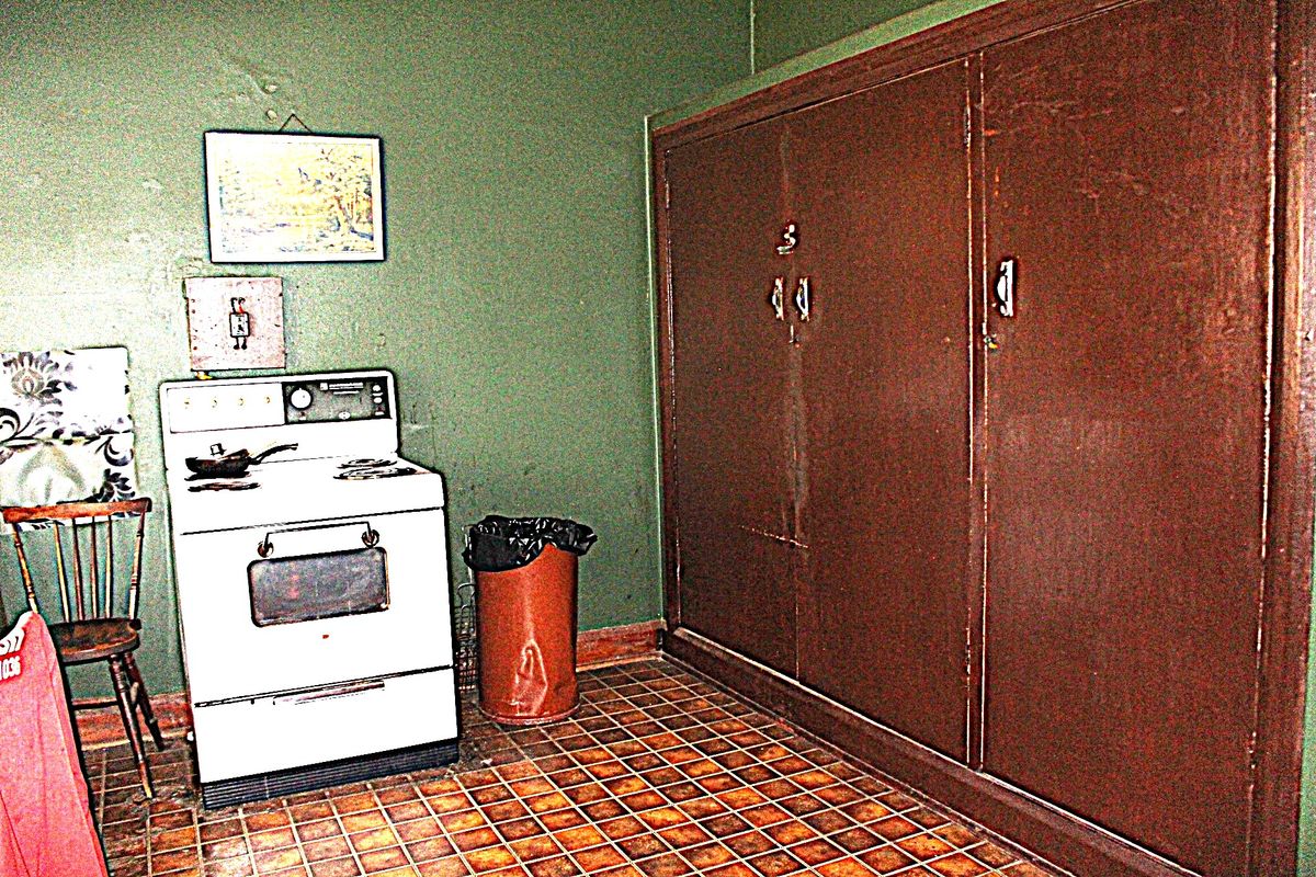 A dated kitchen area featuring built-in cabinetry, a freestanding stove, and tiled flooring, currently requiring significant cosmetic updates and repairs to the wall finishes.