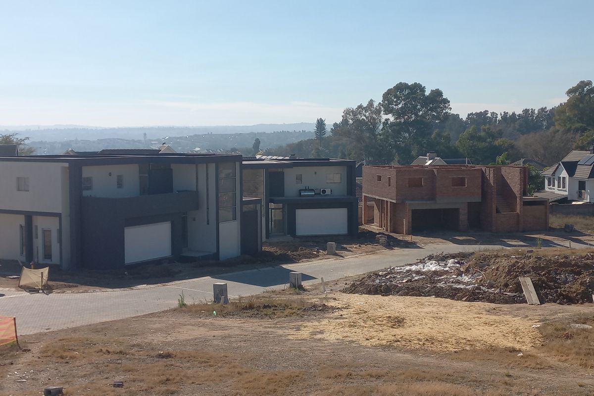 Aerial view of a residential development site featuring completed modern homes alongside an unfinished brick structure and unlandscaped grounds.
