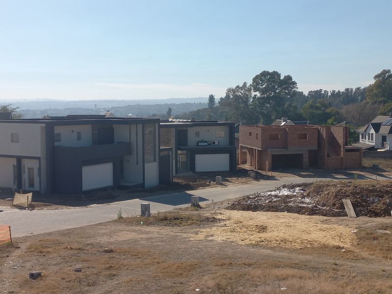 Aerial view of a residential development site featuring completed modern homes alongside an unfinished brick structure and unlandscaped grounds.