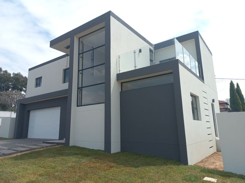 Modern double-story residential home featuring a sleek facade, large feature windows, a glass-railed balcony, and an integrated garage.