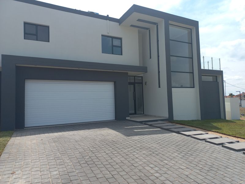 Modern double-storey residential facade featuring a paved driveway, integrated double garage, and striking architectural glass elements.
