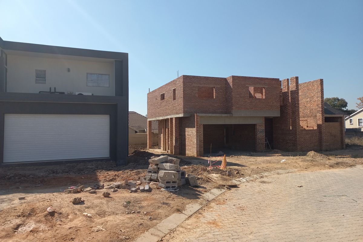 A view of a residential property under construction, featuring an unfinished brick structure alongside a completed modern garage facade.
