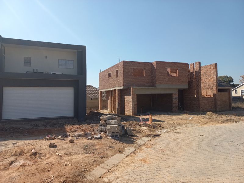 A view of a residential property under construction, featuring an unfinished brick structure alongside a completed modern garage facade.