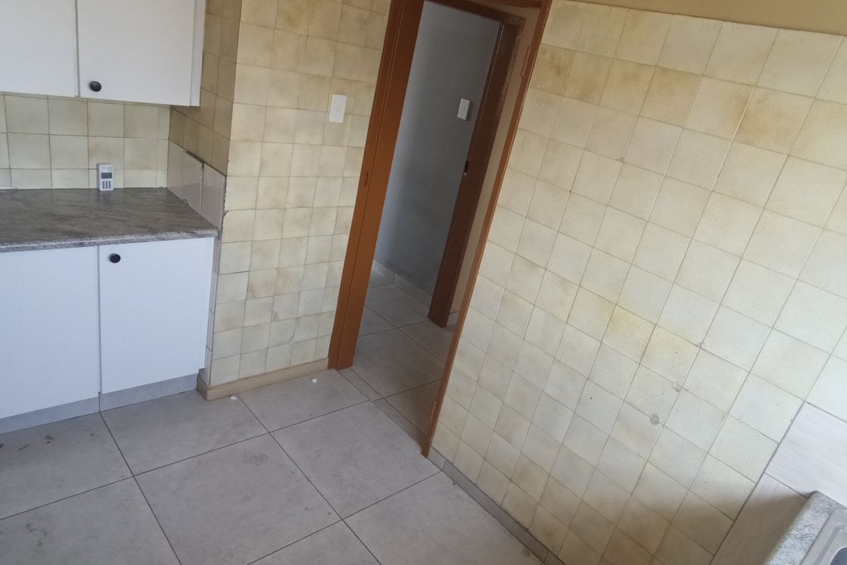 A dated kitchen area featuring built-in cabinetry, laminate countertops, and tiled walls, currently vacant and in need of cosmetic updates.