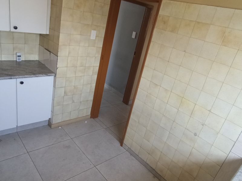 A dated kitchen area featuring built-in cabinetry, laminate countertops, and tiled walls, currently vacant and in need of cosmetic updates.