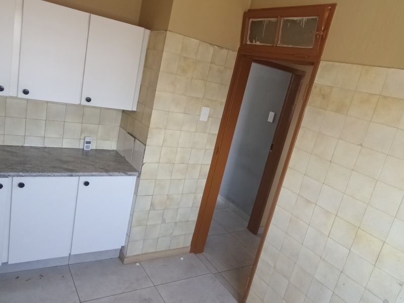 A compact kitchen featuring white built-in cabinetry, laminate countertops, and tiled wall finishes, currently vacant and ready for renovation.