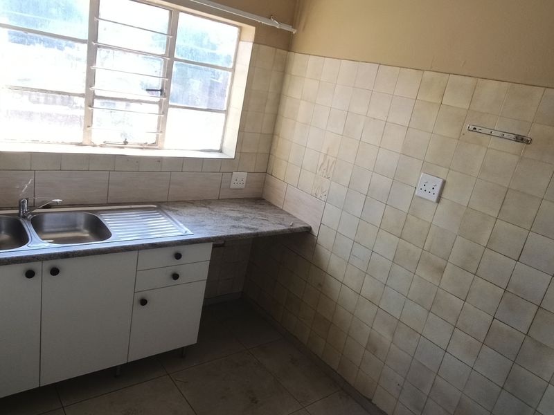 A compact, empty kitchen featuring a double bowl sink, tiled splashbacks, and basic base cabinetry, requiring cosmetic updates to improve its dated appearance.