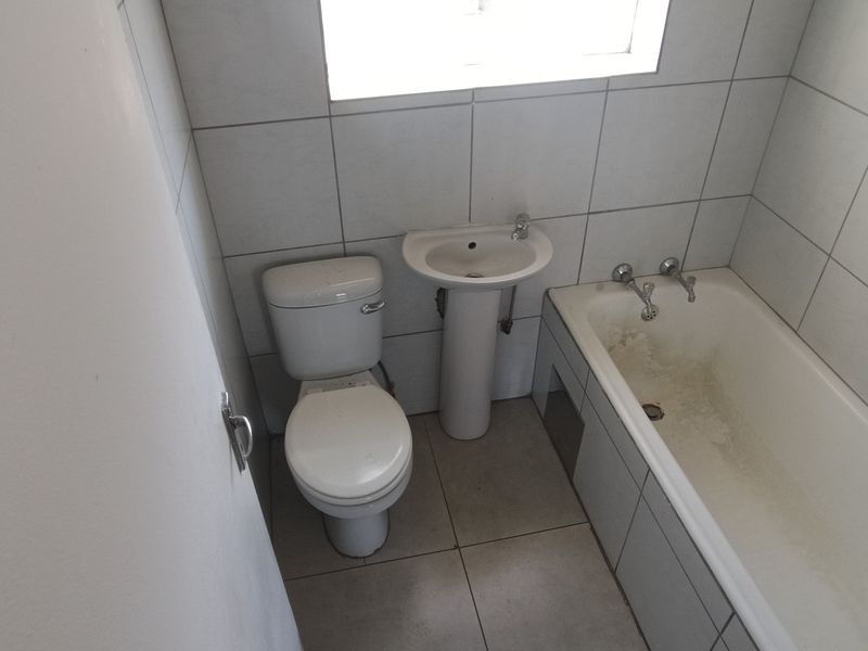 A compact bathroom featuring a pedestal basin, toilet, and bathtub with full-height wall tiling.