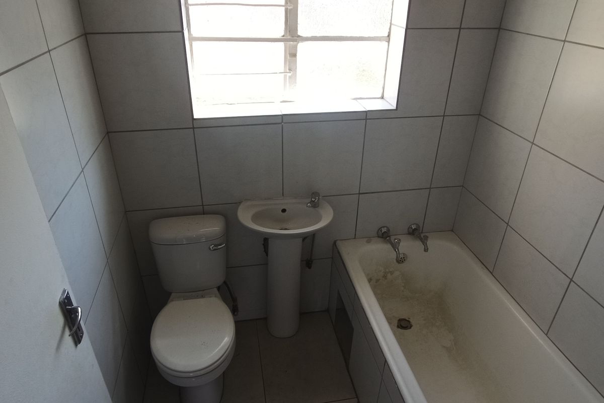 A compact bathroom featuring a pedestal basin, toilet, and bathtub with full-height wall tiling and a window with security bars.