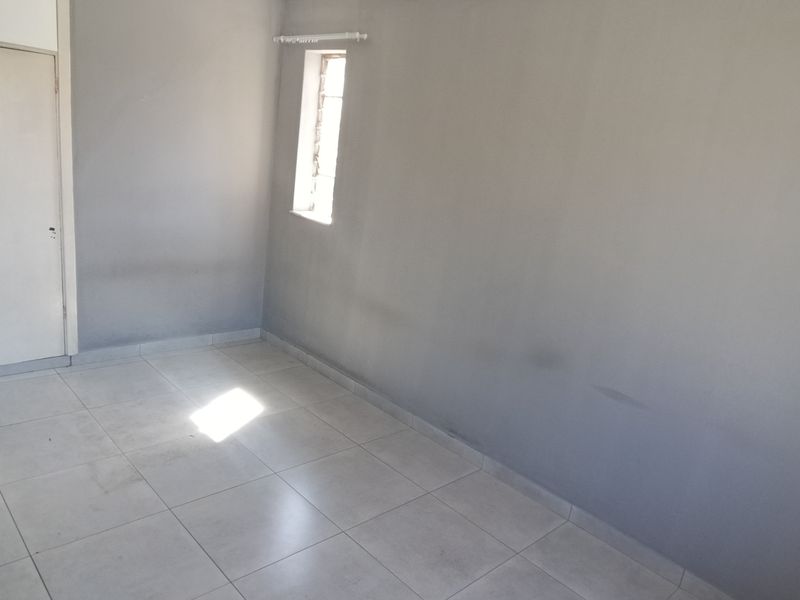 An empty bedroom featuring neutral tiled flooring, a built-in cupboard, and a window with security bars, ready for personalization.
