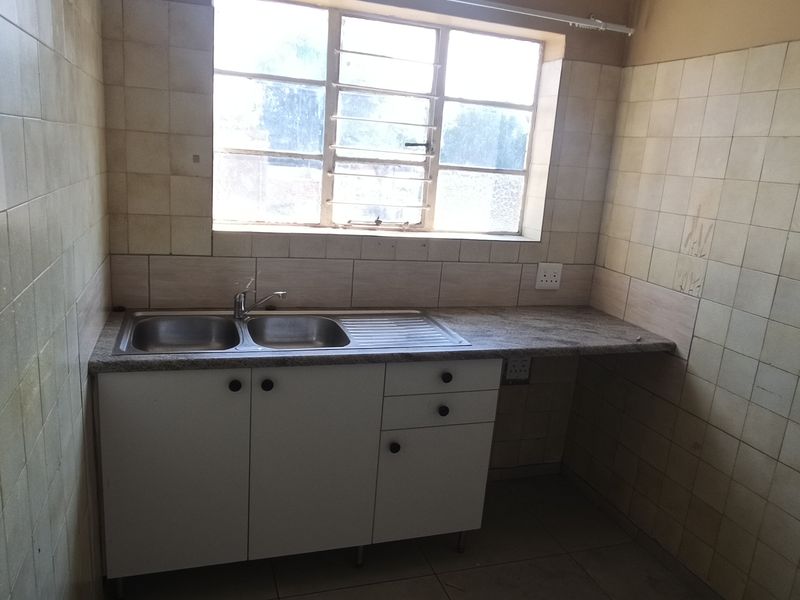 A compact, empty kitchen featuring tiled walls, a double sink, and granite countertops, offering a functional space ready for modernization.