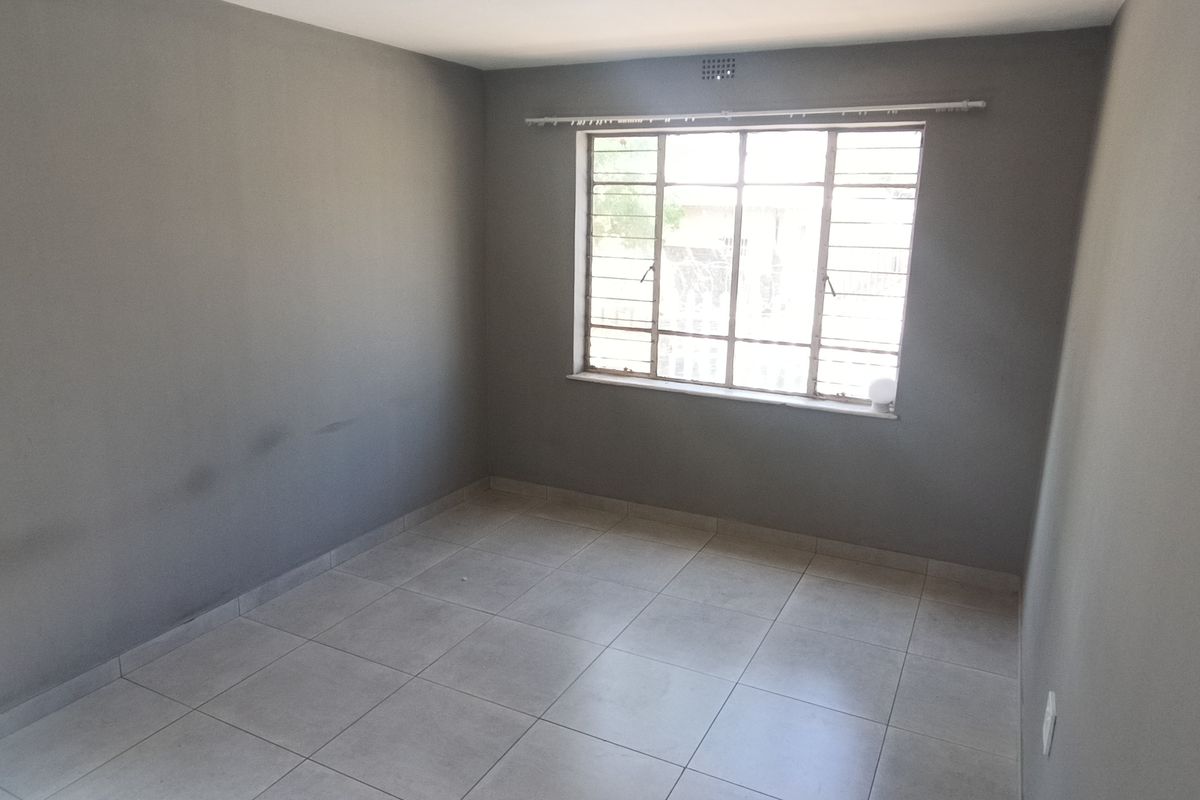 An empty bedroom featuring neutral grey walls, tiled flooring, and a steel-framed window with security bars.