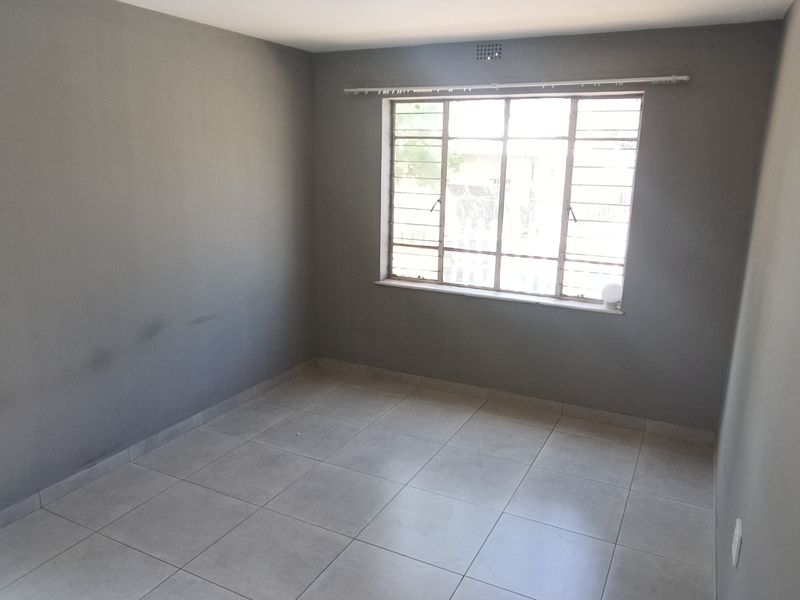 An empty bedroom featuring neutral grey walls, tiled flooring, and a steel-framed window with security bars.