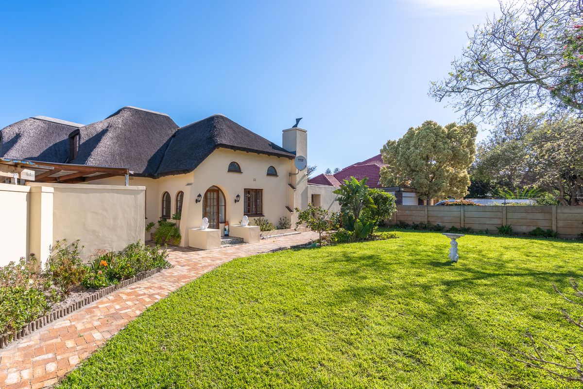 A well-maintained rear garden featuring a charming thatched-roof house, a brick-paved pathway, and a spacious lawn area.