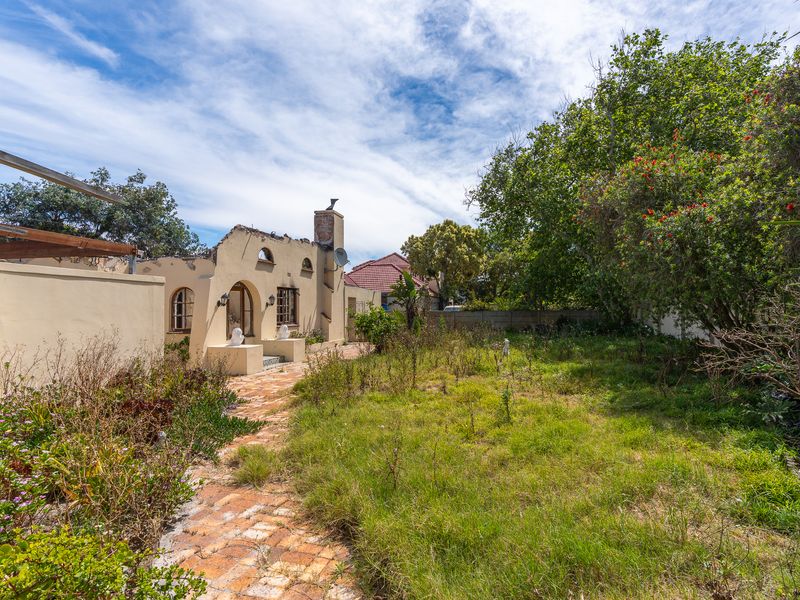 Rear view of the property featuring a brick pathway, overgrown garden, and visible exterior wall deterioration requiring maintenance.