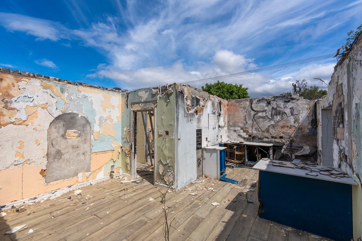A severely damaged kitchen space showing extensive structural deterioration, fire damage, and missing roof, requiring complete renovation or demolition.