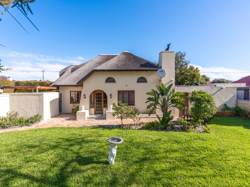 Rear view of a charming house featuring a traditional thatch roof, a paved patio area, and a well-maintained garden with boundary walls.