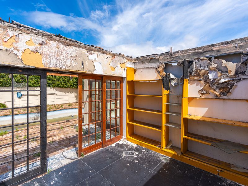 Interior living space showing significant fire damage and structural deterioration, featuring built-in shelving and sliding doors leading to an outdoor pool area.