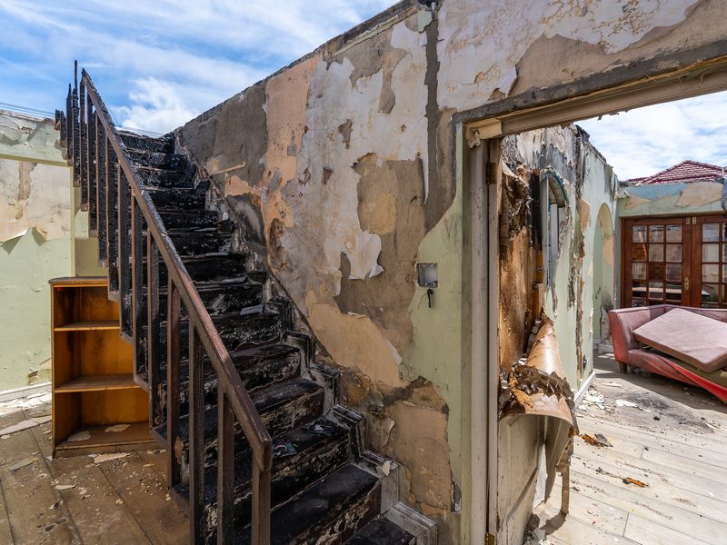 Interior view of a severely fire-damaged living area featuring a charred staircase and extensive wall finish deterioration.