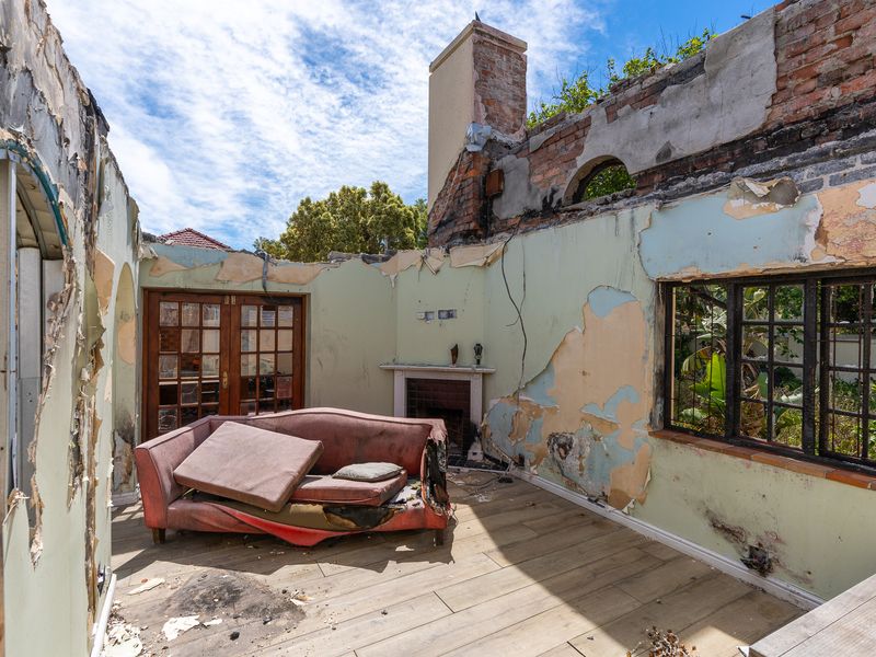 Living room space showing extensive fire damage with exposed brickwork, damaged plaster, and missing roof structure.