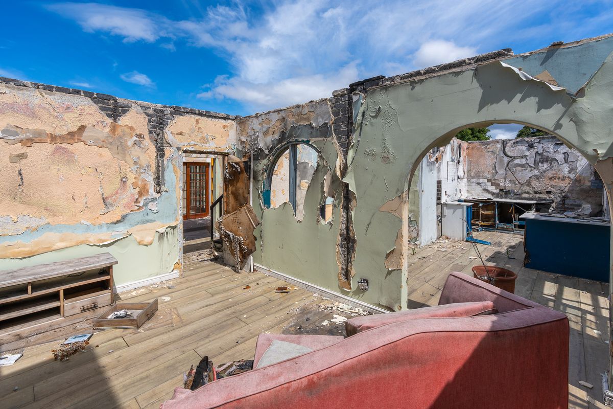 A severely fire-damaged living area showing extensive destruction to walls and finishes, requiring complete structural renovation and restoration.