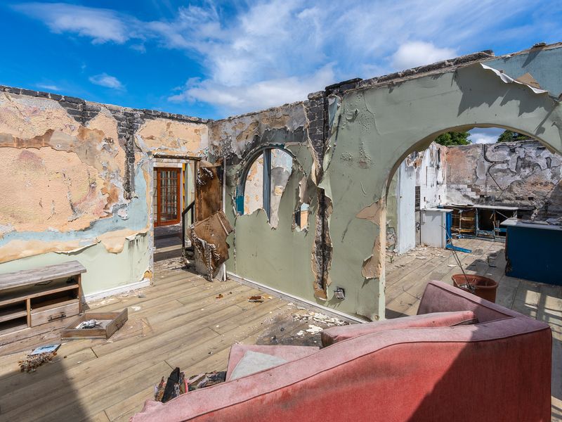 A severely fire-damaged living area showing extensive destruction to walls and finishes, requiring complete structural renovation and restoration.