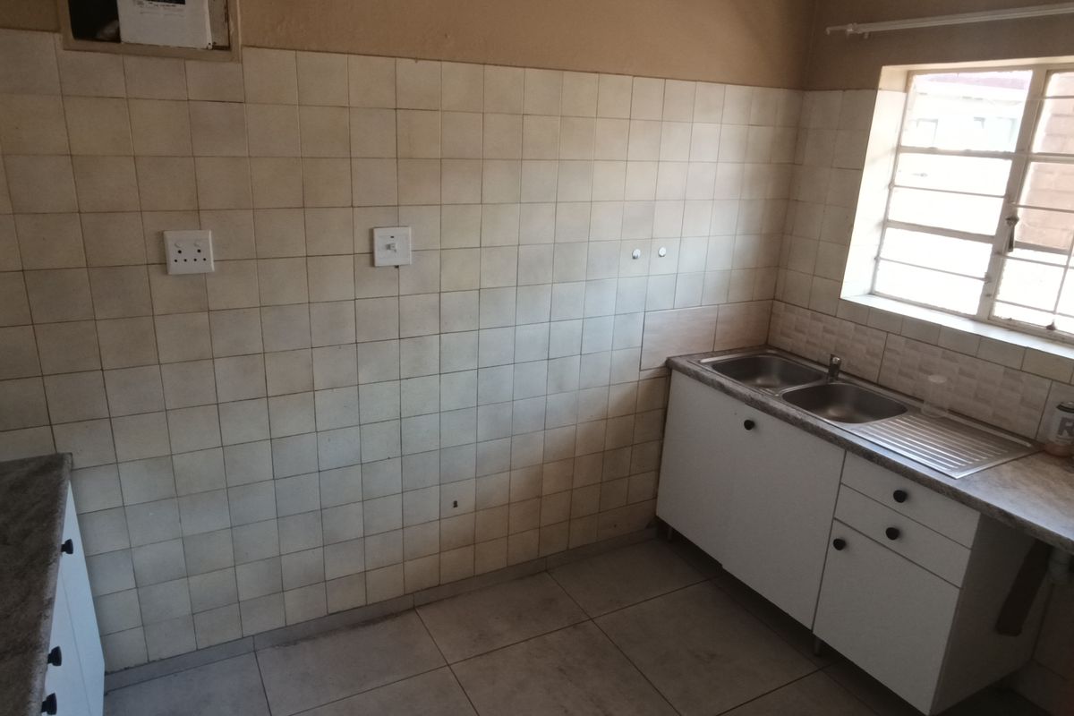 A functional, empty kitchen featuring built-in cabinetry, a stainless steel sink, and tiled splashbacks, offering a blank canvas for potential renovation or modernization.