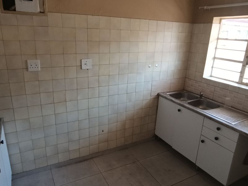 A functional, empty kitchen featuring built-in cabinetry, a stainless steel sink, and tiled splashbacks, offering a blank canvas for potential renovation or modernization.