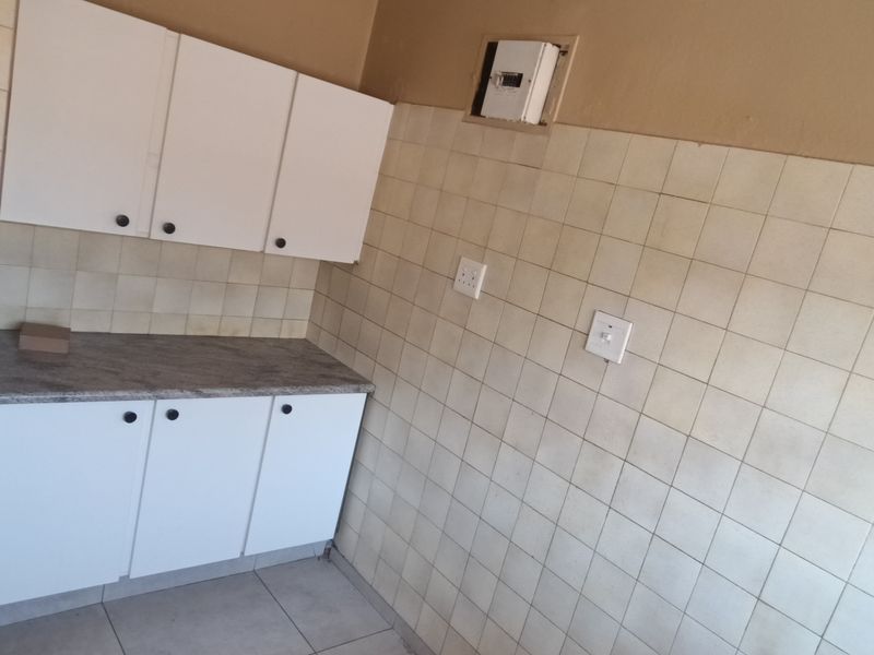 A compact kitchen area featuring white built-in cabinetry, a laminate countertop, and tiled wall finishes, currently presented as an empty space.