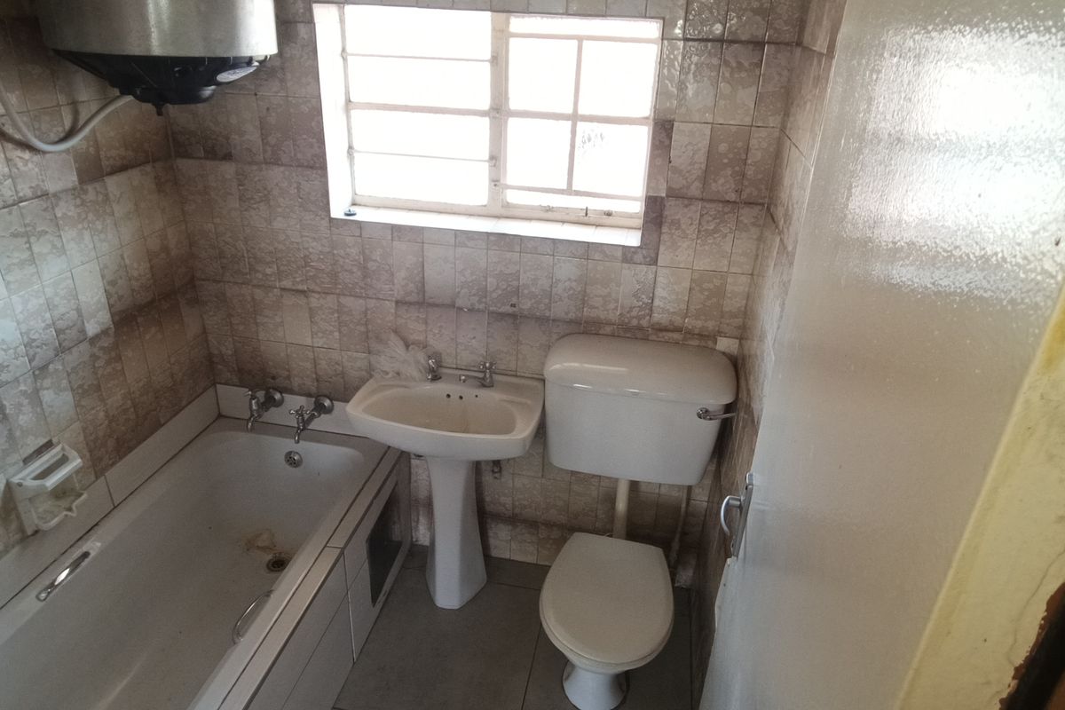 A dated bathroom featuring a bathtub, pedestal basin, and toilet, with wall-mounted geyser and tiled finishes requiring renovation.