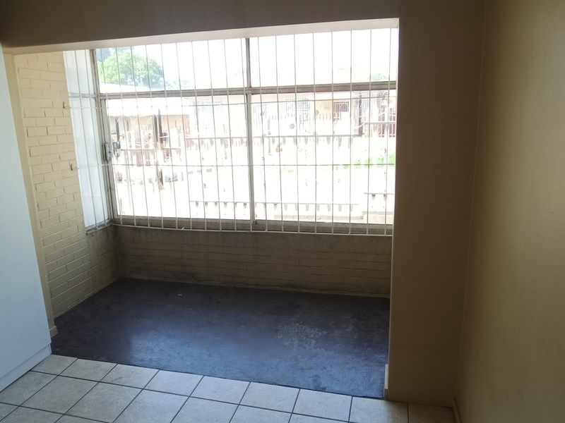 An empty bedroom featuring a built-in wardrobe, tiled flooring, and large windows fitted with security bars.