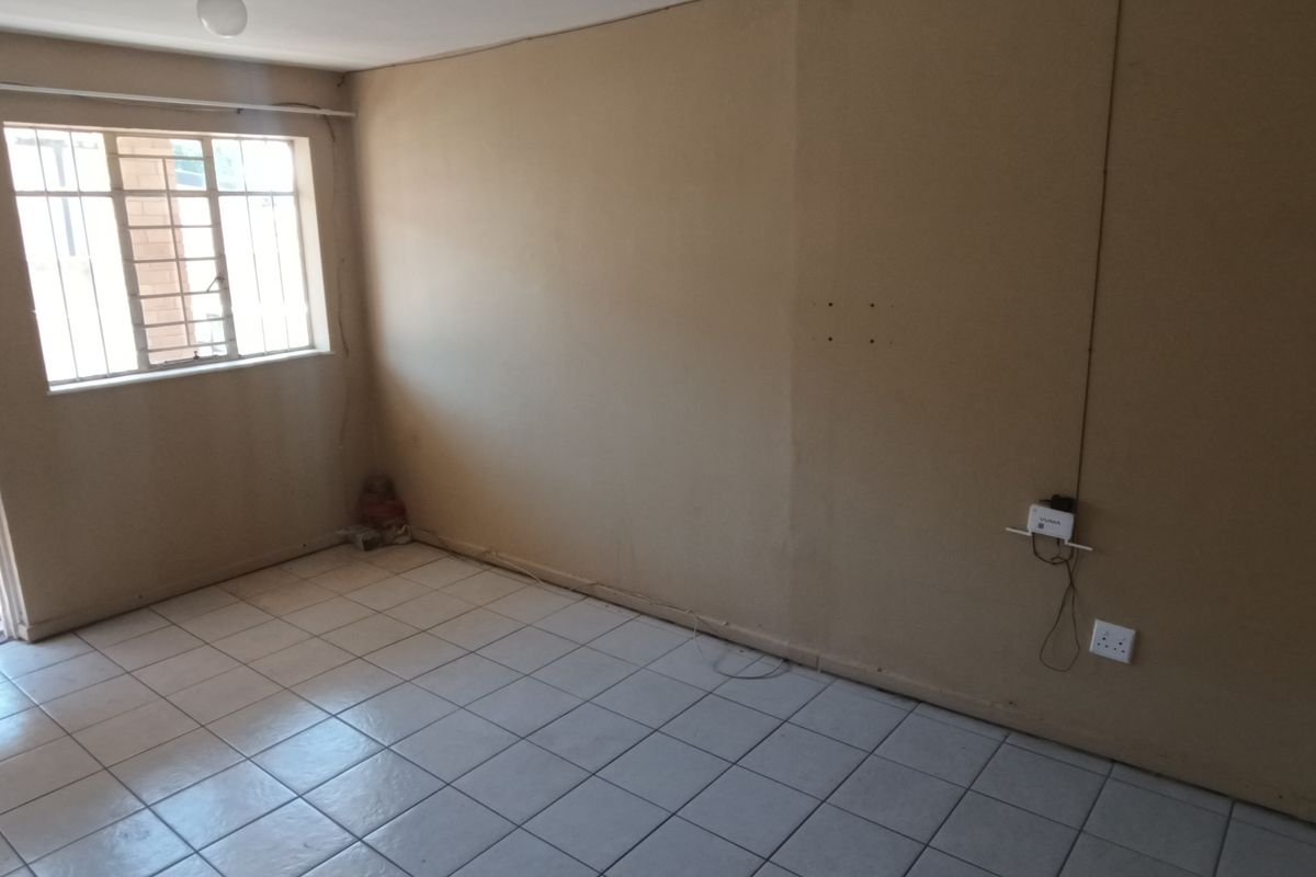 An empty living room featuring tiled flooring, security bars on the windows, and a security gate, providing a blank canvas for renovation.