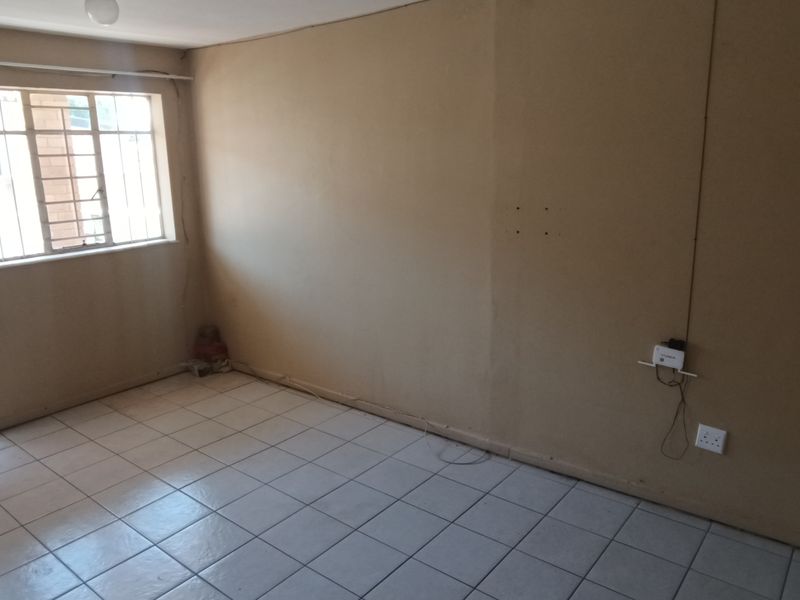 An empty living room featuring tiled flooring, security bars on the windows, and a security gate, providing a blank canvas for renovation.