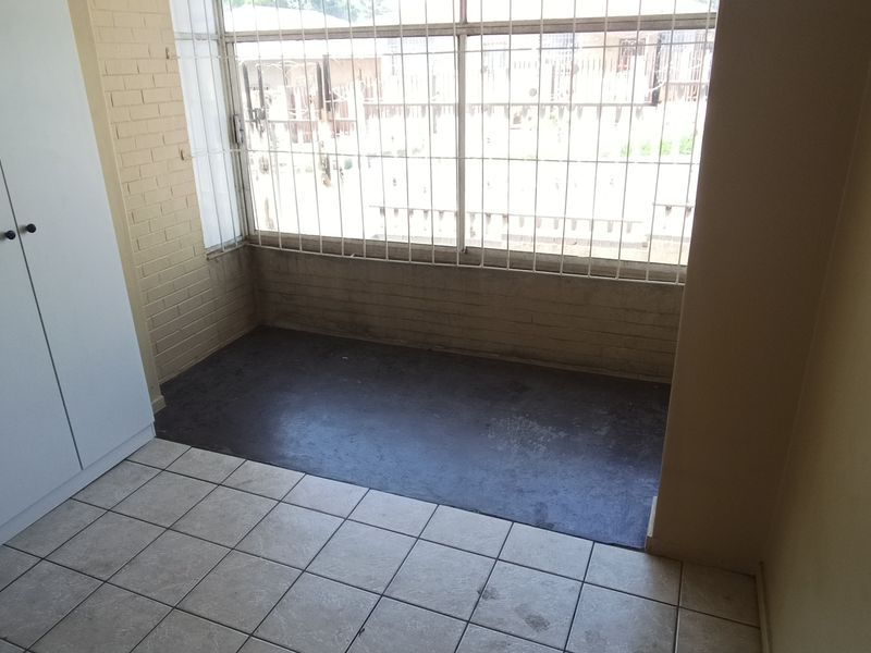 An empty bedroom featuring built-in wardrobes, tiled flooring, and large windows fitted with security bars.