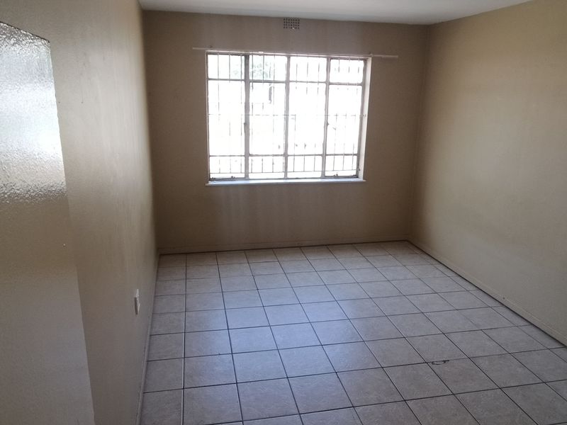 An empty bedroom featuring neutral wall paint, tiled flooring, and a window fitted with security bars.