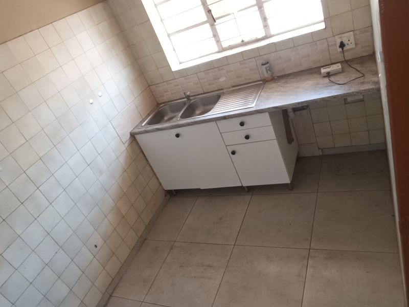 A compact, empty kitchen featuring tiled walls, a stainless steel sink, laminate countertops, and base cabinetry, offering a functional space ready for updates.