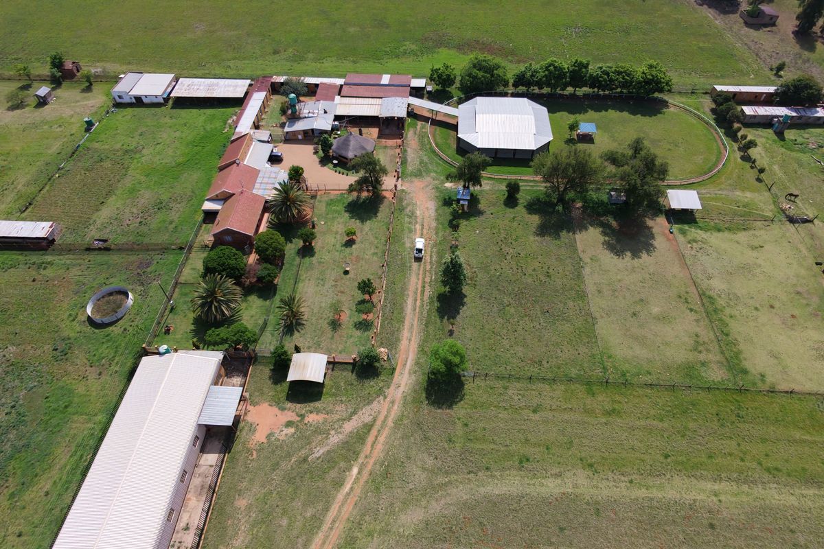 Aerial view of a large rural property featuring multiple outbuildings, extensive fenced paddocks, and a central circular structure on a spacious plot.