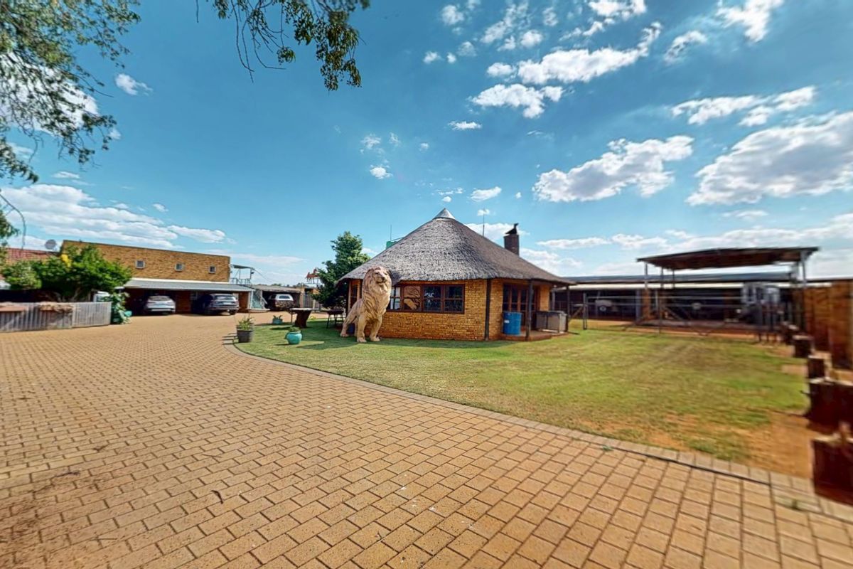 Spacious rear exterior area featuring a traditional thatch-roof building, extensive brick paving, and ample covered parking facilities on a well-maintained property.