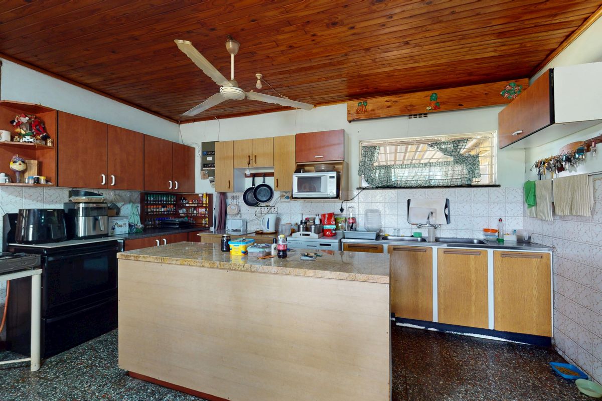 A dated kitchen featuring timber ceilings, a central island with granite countertops, and extensive built-in cabinetry, offering significant potential for a modern renovation.