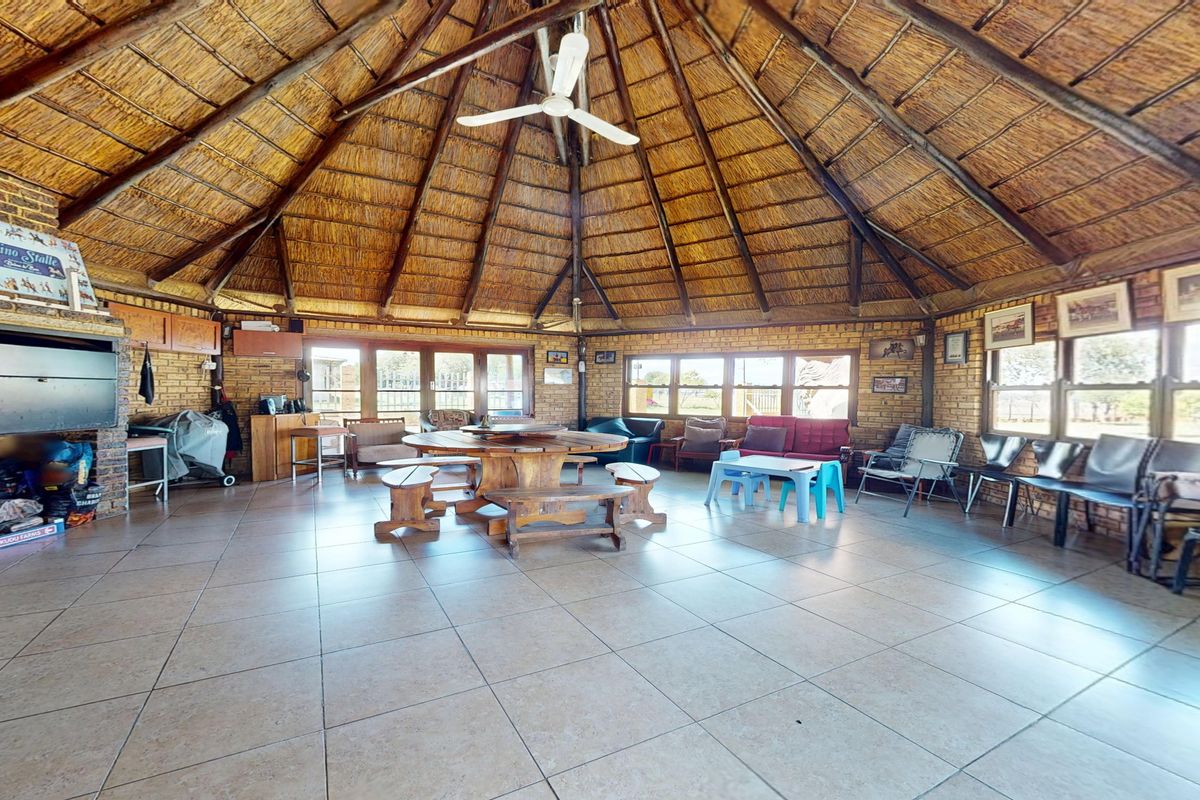 Spacious living area featuring a high thatched roof with exposed timber rafters, brick walls, tiled flooring, and a built-in fireplace.